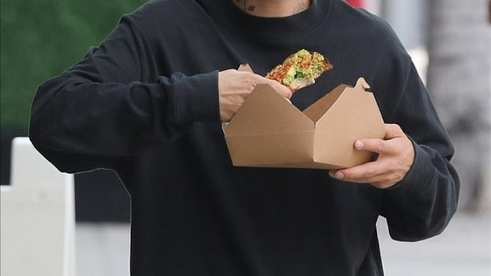 Nam ca sĩ diện set đồ màu đen giản dị, vừa đi vừa ăn pizza ngay trên phố.