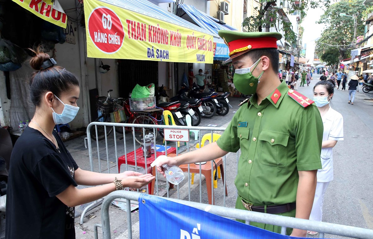 Người dân vào mua đồ thiết yếu tại chợ Đồng Xuân được lực lượng chức năng yêu cầu rửa tay sát khuẩn. (Ảnh: Phạm Kiên/TTXVN)