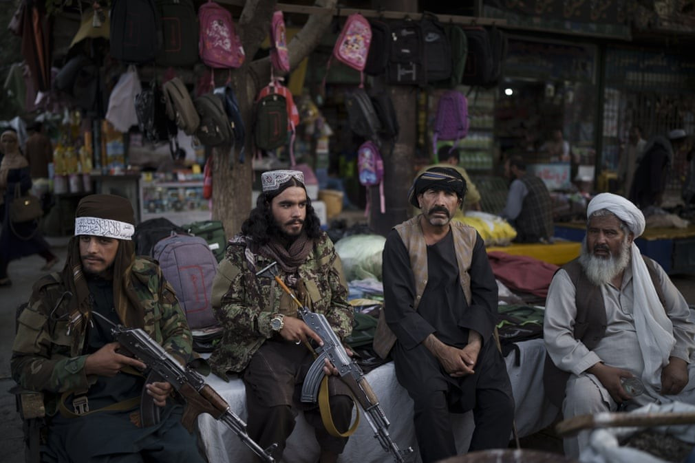 Các chiến binh Taliban ngồi cạnh những người bán hàng rong tại một khu chợ địa phương ở Kabul, Afghanistan. (Nguồn: AP)