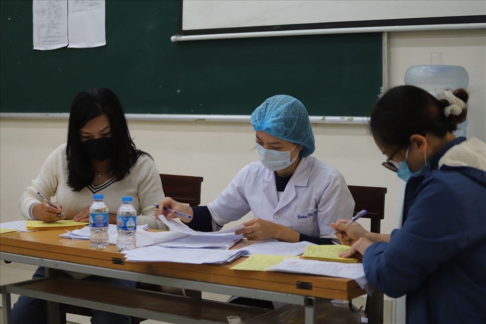 Nhân viên y tế và giáo viên ghi giấy tiêm mũi 1 cho học sinh.